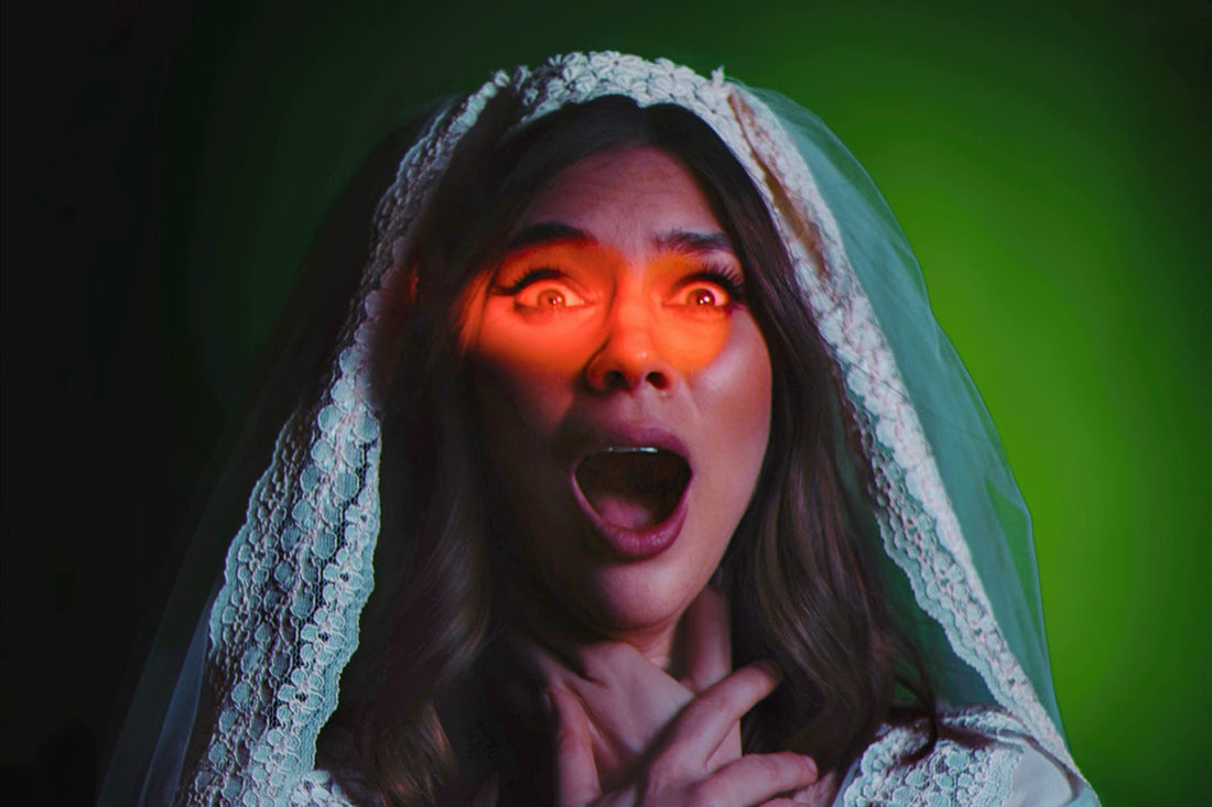Djunah in a white lace bridal veil and gown with a shocked expression, lit by a dramatic red eyelight and green theatrical lighting against a dark background.