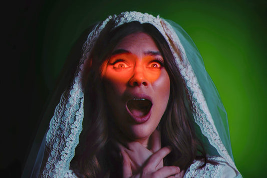 Djunah in a white lace bridal veil and gown with a shocked expression, lit by a dramatic red eyelight and green theatrical lighting against a dark background.