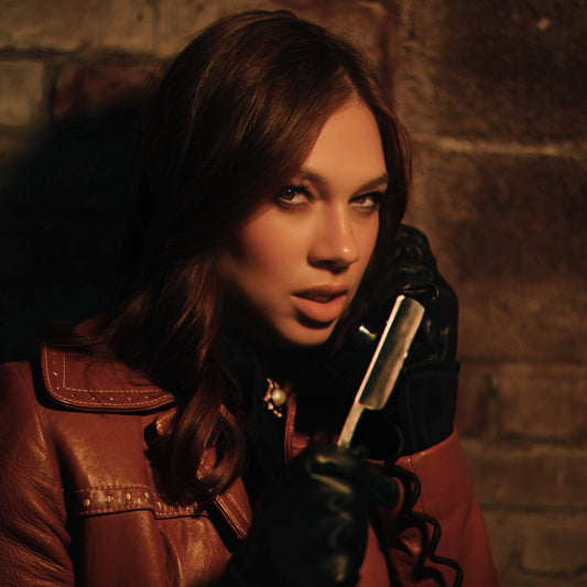 Djunah singer-guitarist Donna Diane holding a straight razor and a telephone, wearing black leather gloves and a brown leather jacket, staring menacingly
