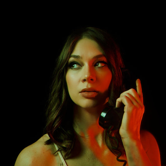 Portrait of a Donna DIane from Djunah holding a black telephone receiver against a dark background, her gaze turned to the side. Dramatic red and green lighting evokes the atmosphere of Italian giallo horror films.